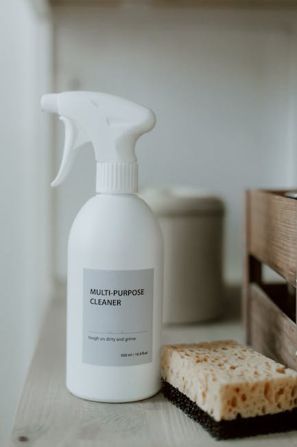 A close-up image showing a white spray bottle labeled 'Multi-Purpose Cleaner' positioned on a light-colored surface, possibly a kitchen or utility area. The bottle is in the foreground, with the trigg